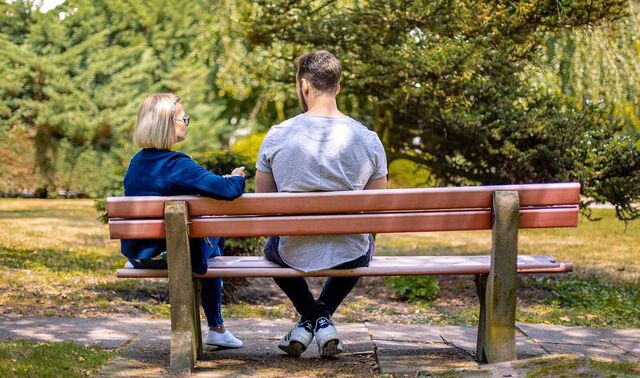 Ein Mann und eine Frau sitzen in einem Park auf einer Bank und unterhalten sich. 